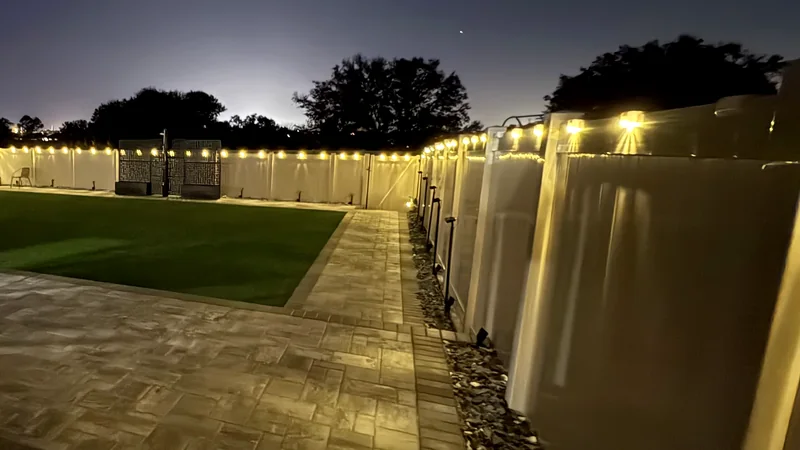 The same backyard after dark with fence lighting on