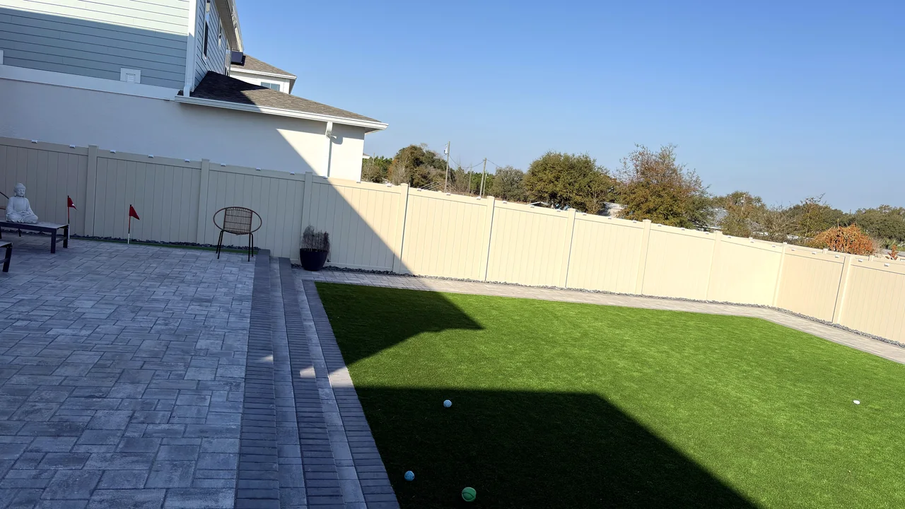 Backyard in daylight: paver walkway, turf lawn and white fence